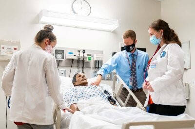 Students and faculty interact with a manikin in a hospital setting